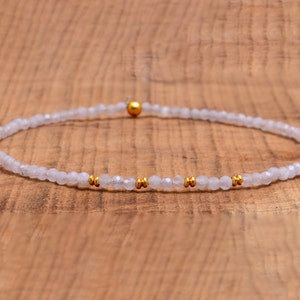 Könnte beinhalten: Ein zartes Armband aus weißen Edelsteinen mit goldenen Akzenten. Das Armband besteht aus kleinen, facettierten Perlen und hat ein schlichtes Design.