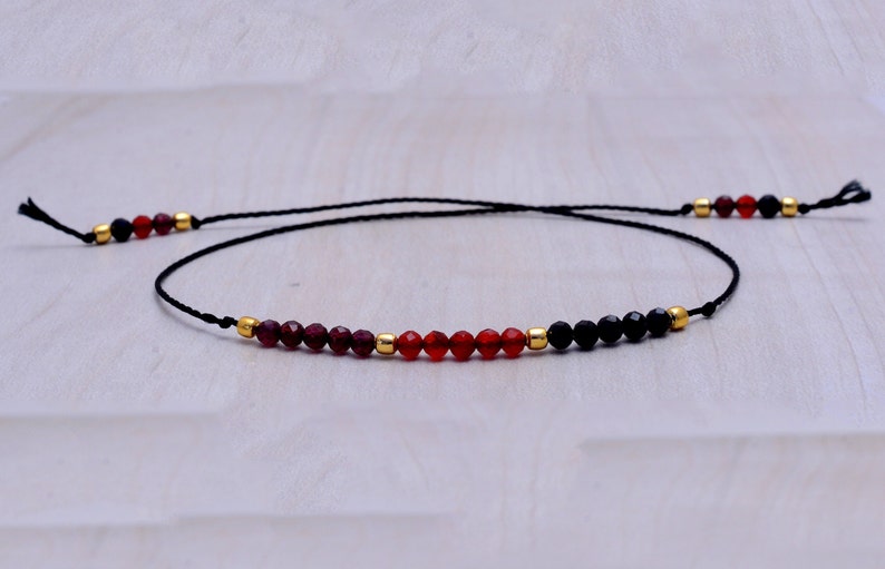 May include: A black string bracelet with red, orange, and black gemstone beads.