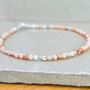 May include: A delicate bracelet made with small, round, white and pink beads with a silver clasp.