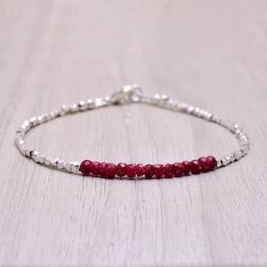 以下が含まれることがあります： 小さな深紅のルビービーズが並んだ、繊細なシルバーブレスレットです。