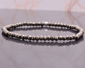 May include: A beaded bracelet composed of small, faceted, metallic gray beads. The bracelet is strung on a flexible cord, forming a continuous loop. The beads have a reflective quality, catching the light and creating a subtle sparkle.