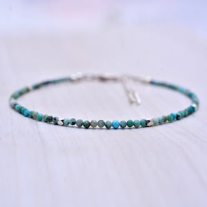May include: A delicate turquoise beaded bracelet with silver detailing. The bracelet is made of small, round turquoise beads, strung together with a silver chain and clasp. The beads are in shades of blue and green.