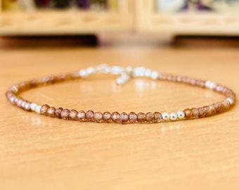 May include: Delicate bracelet featuring small, faceted brown beads interspersed with silver-colored beads. The bracelet is strung on a thin, flexible cord and has a silver clasp. The jewelry is designed for everyday wear.