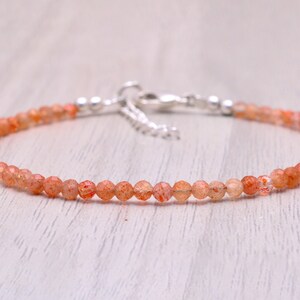 May include: A delicate bracelet featuring small, faceted orange beads. The beads are strung together, creating a subtle sparkle. The bracelet has a silver-colored clasp and chain for adjustable sizing. This jewelry piece is ideal for everyday wear.