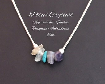 May include: A silver chain necklace with five different colored gemstones. The gemstones are aquamarine, fluorite, turquoise, labradorite, and iolite. The necklace is labeled "Pisces Crystals Aquamarine - Fluorite Turquoise - Labradorite Iolite".