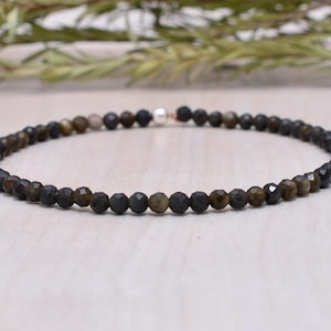 Könnte beinhalten: Ein zartes Armband aus kleinen, dunkelgrünen und schwarzen Edelsteinperlen. Das Armband hat einen silbernen Verschluss.