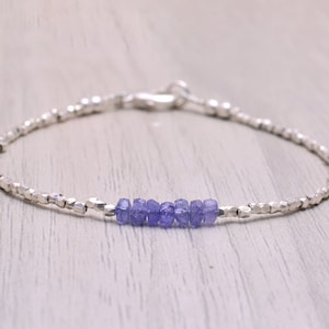 Op de afbeelding: Een delicate zilveren armband met een rij kleine, lichtpaarse edelstenen. De armband is gemaakt van kleine zilveren kralen en heeft een karabijn sluiting.
