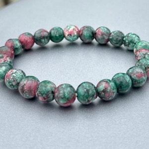 Op de afbeelding: Een armband van groene en roze edelstenen met ronde kralen.