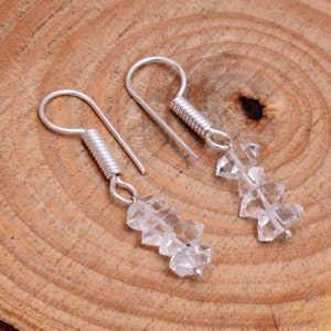 May include: A pair of silver earrings with clear crystal teardrop-shaped charms. The earrings have a spring-loaded hook closure.