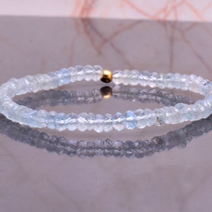 May include: A delicate bracelet made with light blue aquamarine beads and a gold clasp.