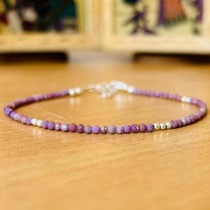 Könnte beinhalten: Ein zartes Armband aus violetten Edelsteinen mit silbernen Akzenten. Das Armband besteht aus kleinen, runden Perlen und ist auf einer silbernen Kette aufgefädelt.