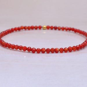 May include: A delicate red gemstone bracelet with small, faceted beads. The bracelet is made with a gold clasp.