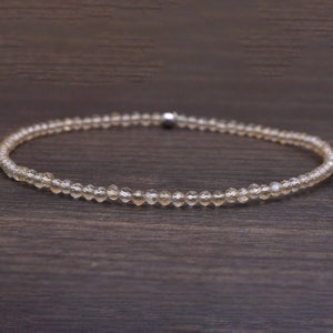 May include: A delicate necklace made of small, clear, faceted beads. The necklace is strung on a silver chain and has a simple, elegant design.
