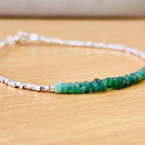 Puede incluir: Un delicado brazalete de cadena plateada con una fila de cuentas de piedras preciosas verdes. Las cuentas están graduadas en tamaño, siendo las más grandes en el centro del brazalete.