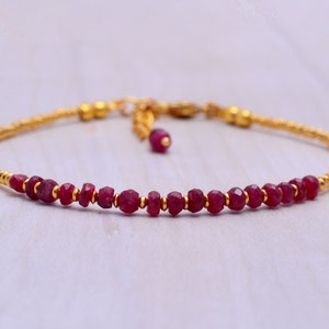 Puede incluir: Un delicado brazalete de oro con una sola fila de pequeñas cuentas de rubí facetadas. El brazalete tiene un cierre deslizante para ajustarlo.
