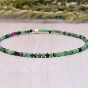 May include: A delicate green, pink, and black gemstone bracelet with a silver clasp.