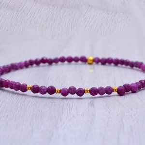 Pode incluir: Um bracelete delicado feito com pequenas contas roxas facetadas e detalhes dourados.