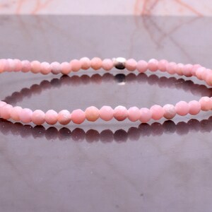 May include: A delicate pink gemstone bracelet. The bracelet is composed of small, faceted, round beads strung together. The beads are a soft, pastel pink color. A silver-colored clasp secures the bracelet.