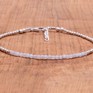 May include: A delicate silver bracelet with a row of white gemstone beads. The bracelet has a silver clasp.