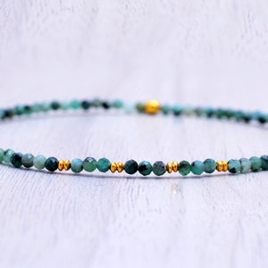 Puede incluir: Un delicado brazalete de piedras preciosas verdes con detalles dorados. El brazalete está hecho de pequeñas cuentas redondas y está enhebrado en una fina cadena dorada.