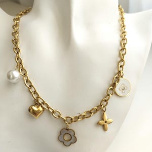 May include: A gold chain necklace with multiple charms, including a pearl, a heart, a flower, and a four-leaf clover. The charms are all gold and have white enamel accents.