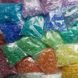 May include: Assortment of small, colourful glass pieces in clear plastic bags. The glass pieces are various shades of blue, green, purple, orange, yellow, and clear.