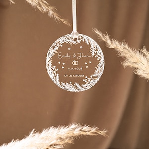 K&ouml;nnte beinhalten: Wei&szlig;er Christbaumschmuck aus Acryl mit floralem Design und dem Text "Emily & John verheiratet 01.01.2023".