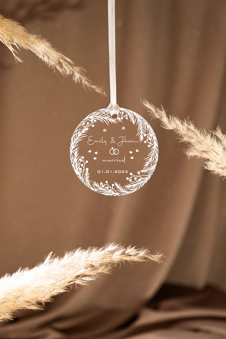 K&ouml;nnte beinhalten: Wei&szlig;er Christbaumschmuck aus Acryl mit floralem Design und dem Text "Emily & John verheiratet 01.01.2023".
