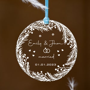 K&ouml;nnte beinhalten: Ein transparenter Glas-Anh&auml;nger mit einem wei&szlig;en Design aus einem Kranz mit Beeren und Bl&auml;ttern. Der Anh&auml;nger tr&auml;gt den Text "Emily & Thron married 01.01.2023".