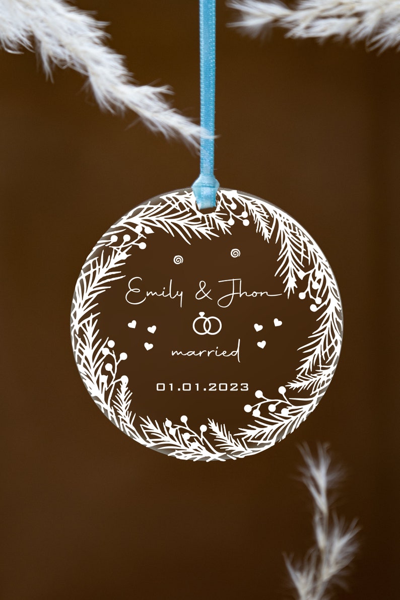K&ouml;nnte beinhalten: Ein transparenter Glas-Anh&auml;nger mit einem wei&szlig;en Design aus einem Kranz mit Beeren und Bl&auml;ttern. Der Anh&auml;nger tr&auml;gt den Text "Emily & Thron married 01.01.2023".