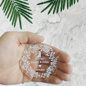 K&ouml;nnte beinhalten: Ein runder, transparenter Acryl-Hochzeitsgeschenkanh&auml;nger mit wei&szlig;em Design. Das Design zeigt ein Paar, ein Herz und den Text "~married~ Laurel & Louis 01.01.2023".