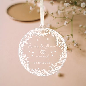 K&ouml;nnte beinhalten: Wei&szlig;er Glasanh&auml;nger mit floralem Design und dem Text "Emily & John verheiratet 01.01.2023"