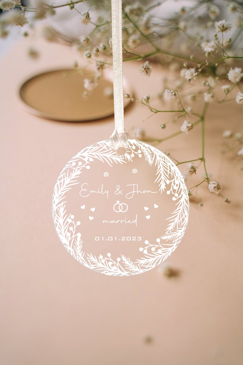 K&ouml;nnte beinhalten: Wei&szlig;er Glasanh&auml;nger mit floralem Design und dem Text "Emily & John verheiratet 01.01.2023"