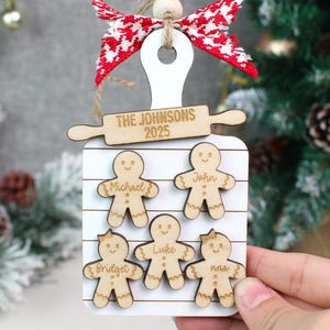 May include: Wooden Christmas ornament shaped like a cutting board with a rolling pin and gingerbread men. The ornament has the text "THE JOHNSONS 2025" and the names Michael, John, Bridget, Luke, and Nora.