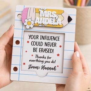 May include: A white wooden frame shaped like a piece of notebook paper with blue lines and three binder holes. A yellow pencil topper features the text MRS. ANDELA. The center displays: YOUR INFLUENCE COULD NEVER BE ERASED! Thanks for everthing you do! From: Hannah.