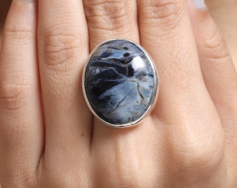Puede incluir: Un anillo de plata con una gran piedra ovalada azul y negra. La piedra tiene un patrón de remolino.