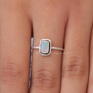 Op de afbeelding: Een zilveren ring met een rechthoekige witte opaal-edelsteen gezet in een bezel-setting. De ringband heeft een getextureerd ontwerp.