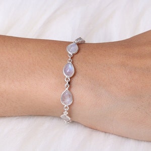 May include: A silver bracelet featuring three pear-shaped, iridescent moonstone gems. The bracelet is connected by small silver links and is displayed on a person's arm.