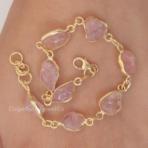 Op de afbeelding: Een goudkleurige kettingarmband met zeven onregelmatige, ruwe, lichtroze rozenkwartsstenen in goudkleurige metalen zettingen. De armband is voorzien van een karabijnsluiting en diverse ringetjes voor verstelling. De tekst luidt ElegantSilverjewelCo.