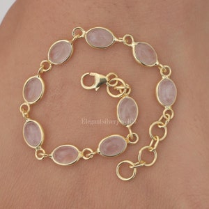 May include: A gold chain bracelet with oval-shaped pink quartz stones. The bracelet has a lobster clasp closure.