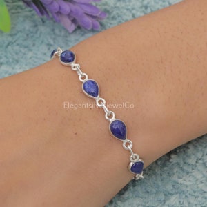 以下が含まれることがあります： チェーンリンクのデザインと涙滴型のラピスラズリストーンが付いたシルバーブレスレット。ブレスレットは手首につけられています。