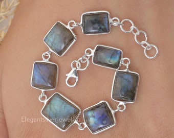 May include: A silver link bracelet featuring six rectangular labradorite gemstones with iridescent blue and grey flashes. The bracelet includes a lobster claw clasp and an adjustable chain extension. The text ElegantSilverJewelCo is visible.