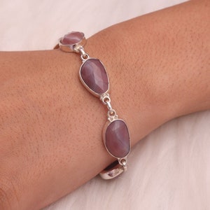 May include: A silver bracelet with four oval-shaped, purple gemstones. The bracelet is on a person's wrist.