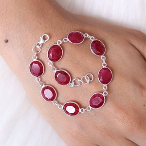 May include: A silver bracelet with oval-shaped red gemstones. The bracelet has a lobster claw clasp.