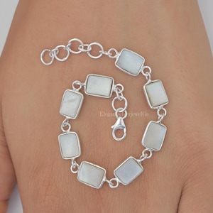 Könnte beinhalten: Ein silbernes Armband mit rechteckigen Steinen aus weißem Perlmutt. Das Armband hat einen Karabinerverschluss.