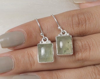 May include: A pair of rectangular drop earrings featuring light green, translucent stones set in polished silver bezels. Each earring hangs from a simple silver hook, showcasing a smooth, flat surface with subtle natural inclusions within the stone.