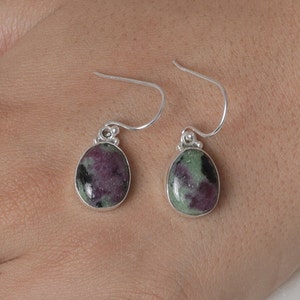 Könnte beinhalten: Ein Paar silberne Ohrhänger mit ovalen, grün-violetten Edelsteinen.