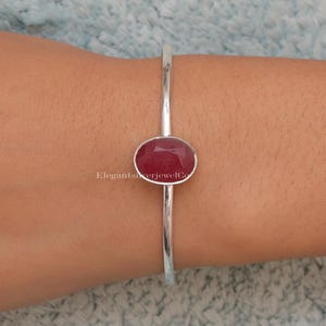 May include: A silver bangle bracelet with a red oval gemstone set in the center.