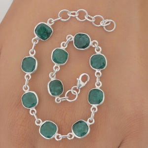 May include: A silver chain bracelet featuring eight square-cut, dark green emerald gemstones set in individual silver bezels. The bracelet includes a lobster claw clasp and an adjustable extender chain with circular links at the end.