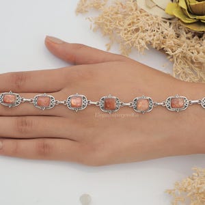 May include: A silver link bracelet featuring seven rectangular sunstone cabochons set in ornate metal frames. The bracelet includes a lobster claw clasp and a series of circular jump rings for adjustable sizing, showcasing a metallic, shimmering orange-brown stone texture.